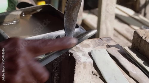 Old hand rubber worker sharpening tapping knife blade whetstone outdoors, manual tool care and precise motion close up rural rustic workshop