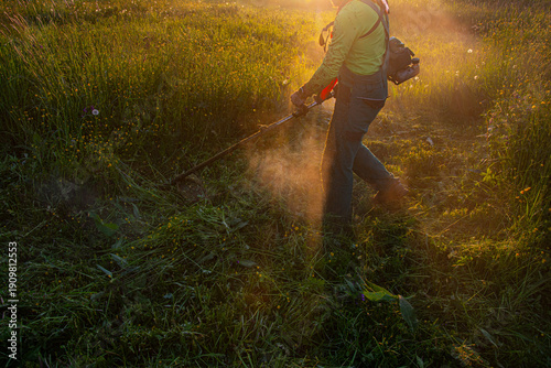 Worker Cutting Grass with Brush Cutter at Sunset