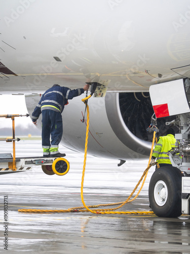Airport ground crew workers connecting external power supply cable to a commercial airplane