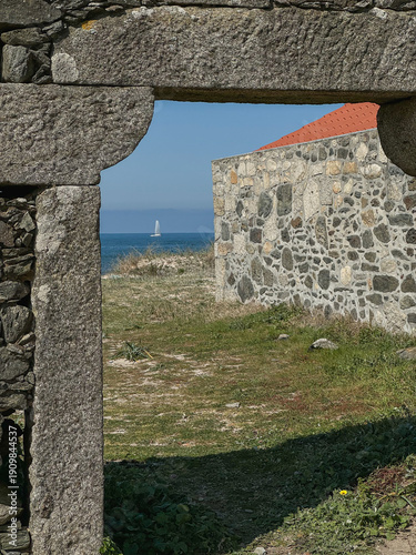 Fotografie Stone gateway framing coastal landscape near Praia De Paco in Carreco, Caminha, Portugal with traditional masonry, red roof house
