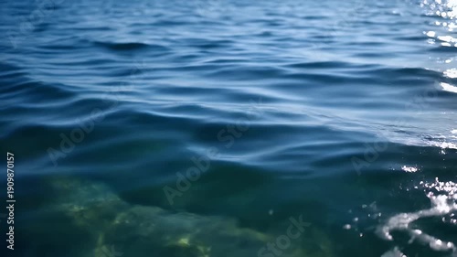 A close-up view of clear blue water with sunlight reflecting on its surface and the seabed visible below