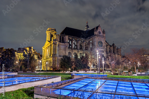 Saint-Eustache church in Paris at night. Gothic architecture and flying buttresses viewed from Nelson Mandela Garden with illuminated blue glass skylights of the Forum des Halles underground complex