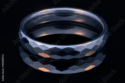 Foto A lit faceted tungsten ring on a black glossy surface.