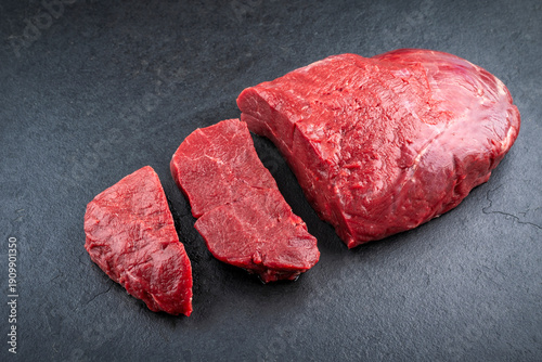 Boneless venison haunch - top round steak raw offered as close-up on slate plate