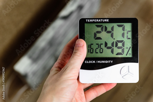Cuadro en lienzo Hand checking room temperature and humidity on a digital thermometer near a heating radiator