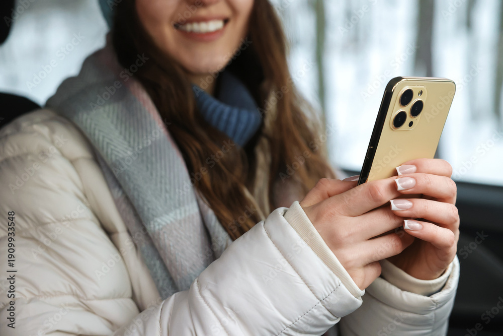 Fototapeta premium Woman with smartphone in car at snowy forest, closeup