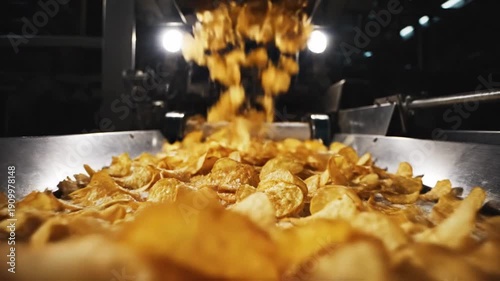 Golden potato chips falling onto a metal conveyor belt in a food processing factory