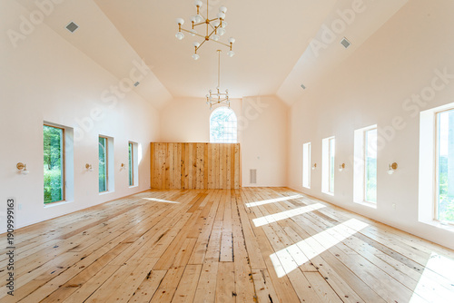 Renovated barn interior with vaulted ceiling and wide plank wood floors, bright minimalist open space with tall windows and modern chandeliers