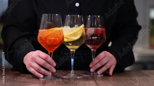Bartender revealing three colorful citrus cocktails on wooden bar counter in elegant sparkling stem glasses