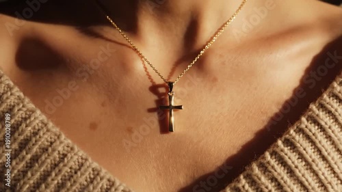 Closeup of a person wearing a gold necklace with a cross pendant set against a knitted sweater