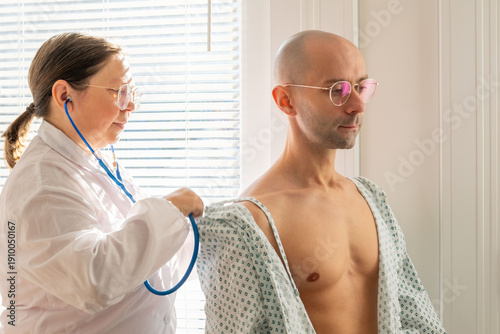 Tableau sur toile female doctor using stethoscope listen male patient's chest, doctor performing a