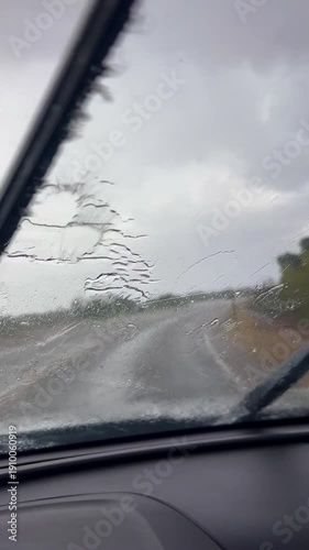 Vertical shot of a car driving down an isolate road during heavy rainfall. Windshield wipers going at high speed.