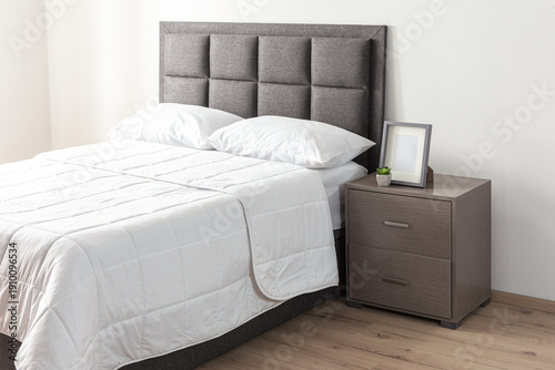 Interior of a modern bedroom with a grey bed featuring a cozy blanket and a wooden bedside table, padded headboard
