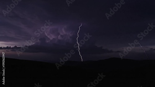 Dramatic lightning strikes illuminate dark mountain silhouettes during a storm.