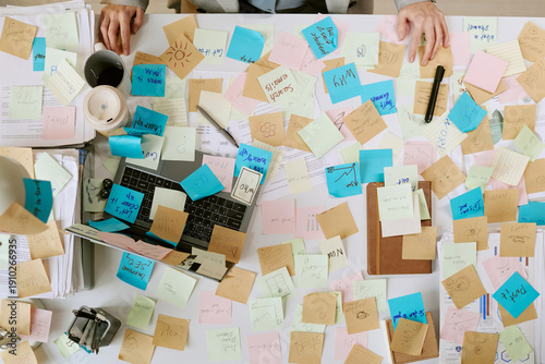 Bilde på lerret Caucasian young adult woman working at cluttered office desk covered with colorf
