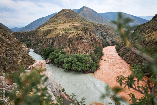 Two rivers with clear and muddy water merge in a mountainous canyon landscape. Meeting of waters phenomenon for ecology and travel concept.