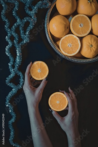 Fresh oranges held in hands near a bowl of oranges on dark background