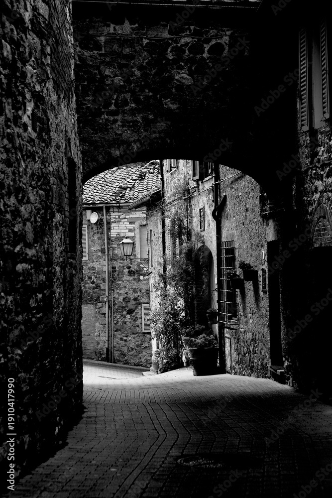 Fototapeta premium Borghi toscani in bianco e nero. L'architettura medievale dei borghi toscani, caratterizzata da pietra, cotto, riflette il periodo comunale con cinte murarie, torri, vicoli stretti e piazze. Italia. 