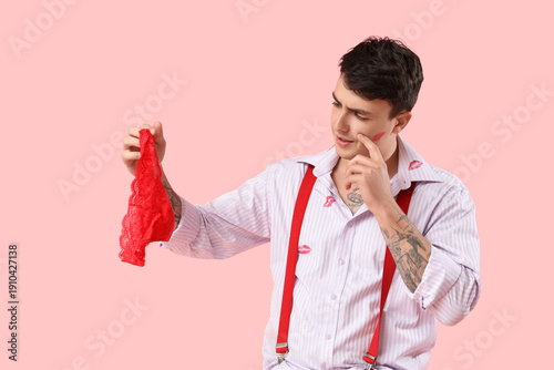Photography Thoughtful man with kiss marks on his shirt and female panties against pink back