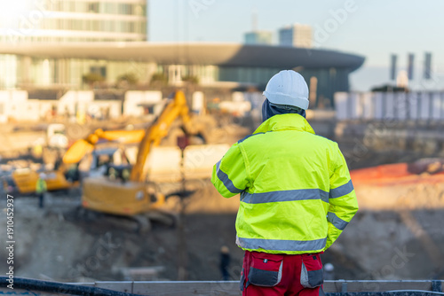 Quadro em tela Construction worker in high visibility jacket and hard hat overseeing excavator