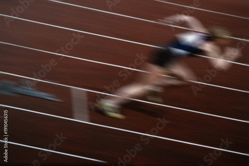 Obraz na plátně Authentic 35mm film scan of track sprint start with motion blur, woman athlete exploding from blocks, grainy analog sports photography