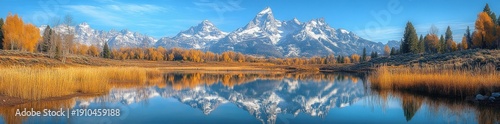 Snow-capped mountain peaks mirrored in a calm reflective lake framed by golden autumn trees and reeds under a clear blue sky, evoking serene and majestic tranquility