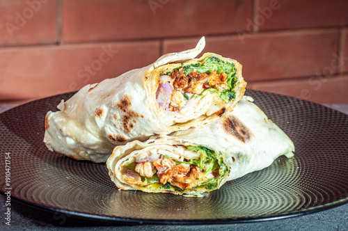 Tortilla przekrojona na pół ze świeżą sałatą i kurczakiem na czarnym talerzu