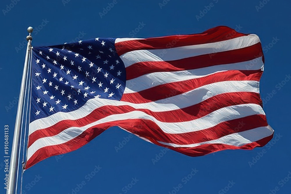 Obraz premium large american flag with stars and stripes waving proudly on a metal flagpole against a clear blue sky