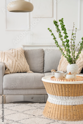 Comfortable sofa, coffee table and vase with blossoming branches in beautiful living room