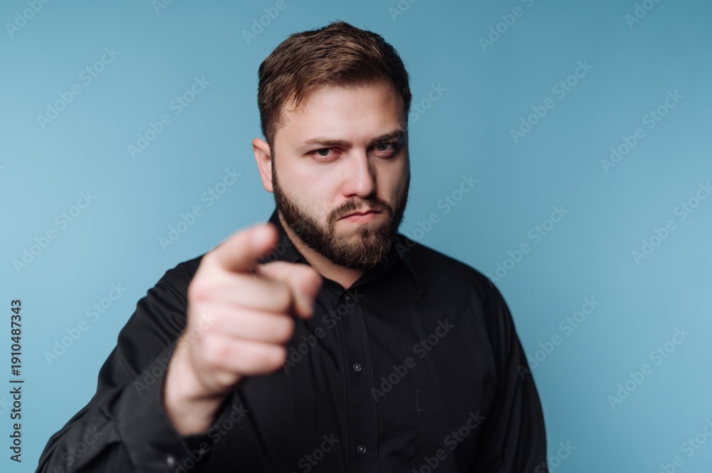 Obraz premium Confident man pointing directly at the viewer with a serious expression against a soft blue background