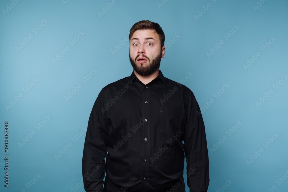 Obraz premium Expression of surprise captured in a modern studio setting with a blue backdrop featuring a man in a black shirt