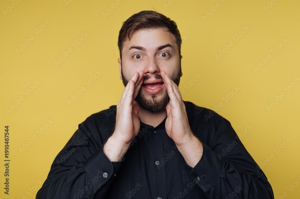 © bodnarphoto - Man joyfully expressing excitement with hands cupped around his mouth in front of a bright yellow backdrop during a lively moment