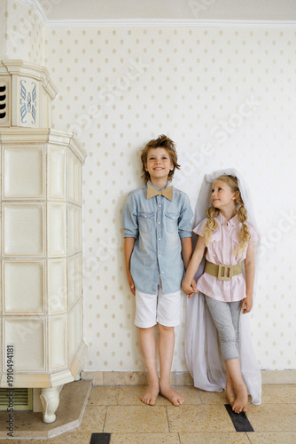 Dressedup boy and girl standing hand in hand at a wall