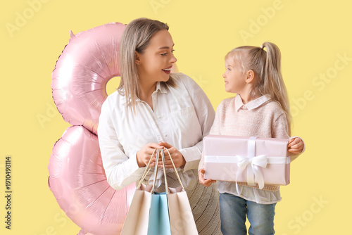 Little girl with her mother, gifts and balloon in shape of figure 8 on yellow background. International Women's Day