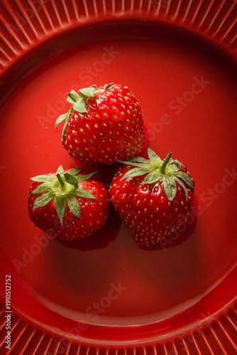 Three fresh strawberries on a red plate