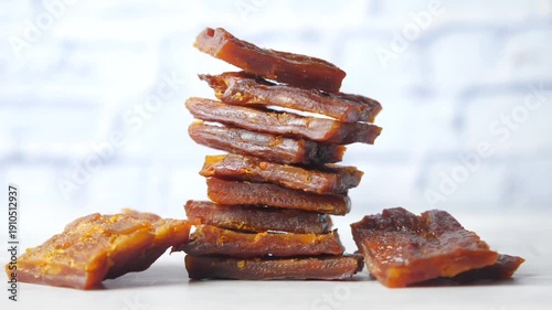 Close up cinematic footage of dried persimmon pieces stacked on a white table with a blurry white brick wall in the background a traditional asian sweet snack