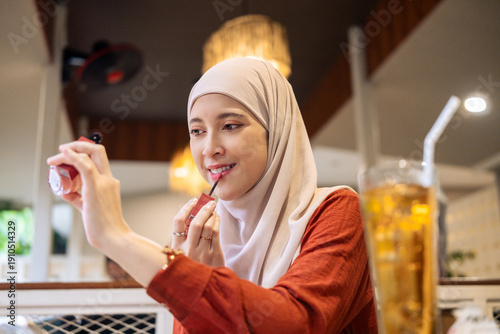 Tableau sur toile Relaxed Woman In Hijab Applying Lipstick At Café Table