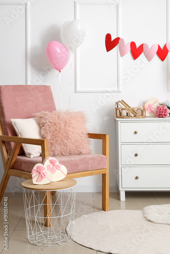 Interior of light living room decorated for Valentine's Day with armchair, drawers and balloons