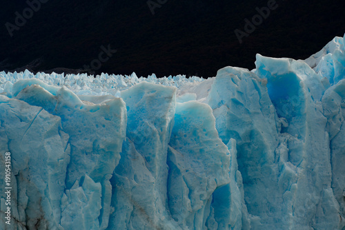 View of a colossal, textured glacier face with striking blue hues against a dark sky, an icy behemoth in Los Glaciares National Park, Santa Cruz Province, Argentina.