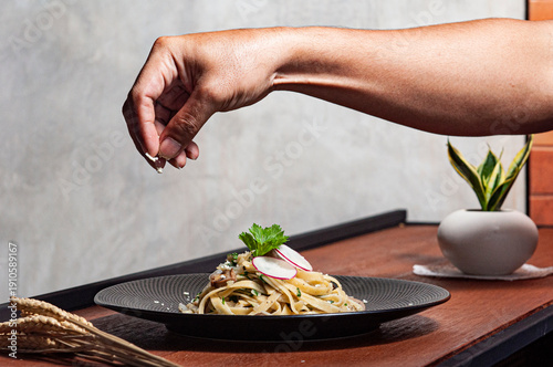 Przyprawianie parmezanem tagiatelle z rzodkiewką, świeżą pietruszką i limonką na czarnym talerzu stojącym na stole