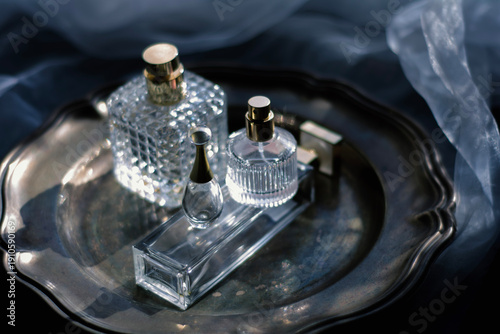 Moody luxury still life of elegant crystal and glass perfume bottles with gold accents arranged on a dark metallic tray. glamour for beauty, fragrance, and high-end lifestyle