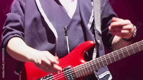 Man with bass guitar claps hands while walks along stage closeup. Positive musician performs with band in night club at festival show