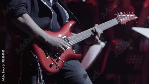Guitarist intently focused on playing striking electric guitar under subtle stage lighting. Live concert setting emphasizes joy of music