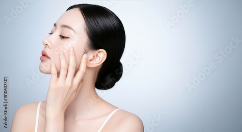 グレー背景で横顔を見せる若い女性のビューティーポートレート、なめらかな素肌に触れる指先が印象的なスキンケア・保湿化粧品広告向けイメージ、AI