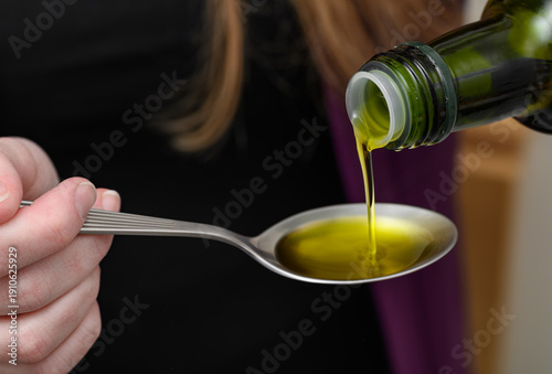 Woman pouring healthy olive oil onto a spoon, a daily dose of healthy omega 3, 6 fatty acids