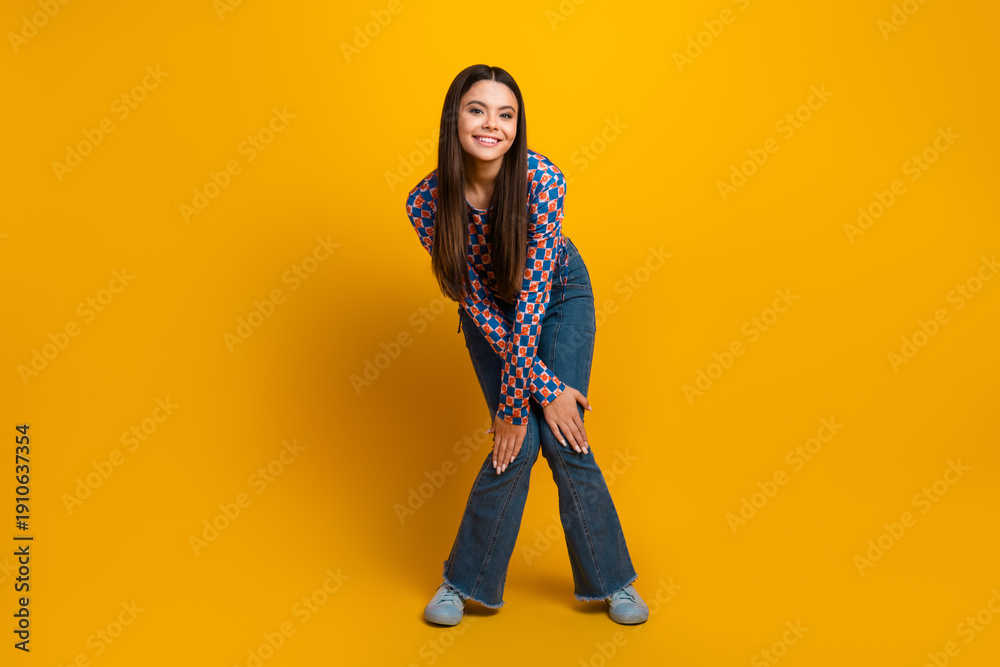 Obraz premium Young stylish Latina teen smiling in a yellow studio wearing a patterned top and jeans in a casual fashion shoot