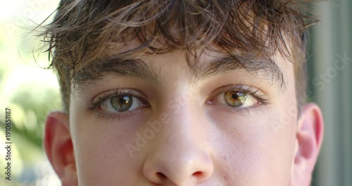 Teenage male blinking and refocusing eyes toward camera near window, reacting to daylight to focus