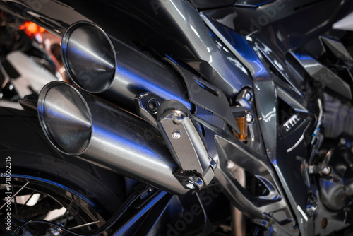 Detail of the dual stainless steel exhaust system, with structural mounts and partially visible spoked rear wheel.