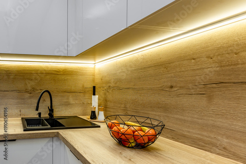 Modern wooden countertop in the kitchen, black sink, salt and pepper shakers, under-cabinet LED lighting in the kitchen