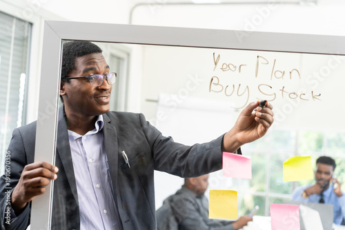 A black businessman wrote on a glass whiteboard about his year plan to buy stock.
